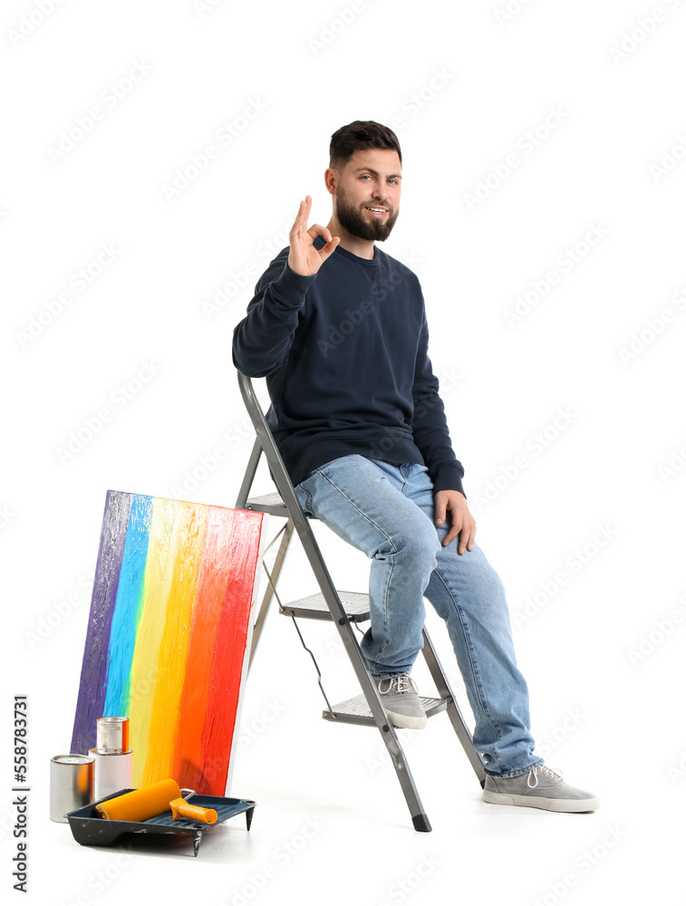 Young man with ladder and painting showing OK on white background