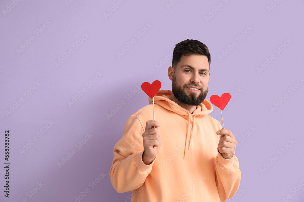 Young bearded man with paper hearts for Valentines Day on lilac background