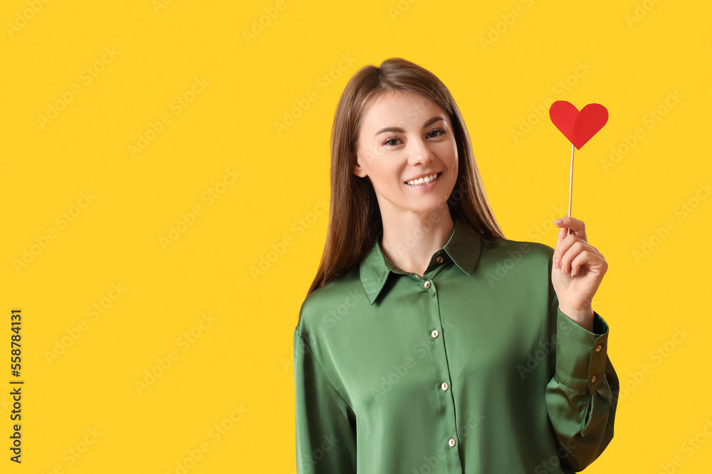 Young woman with paper heart for Valentines Day on yellow background