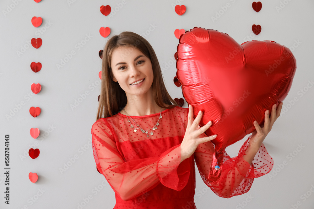 Young woman with balloon for Valentines Day on grey background