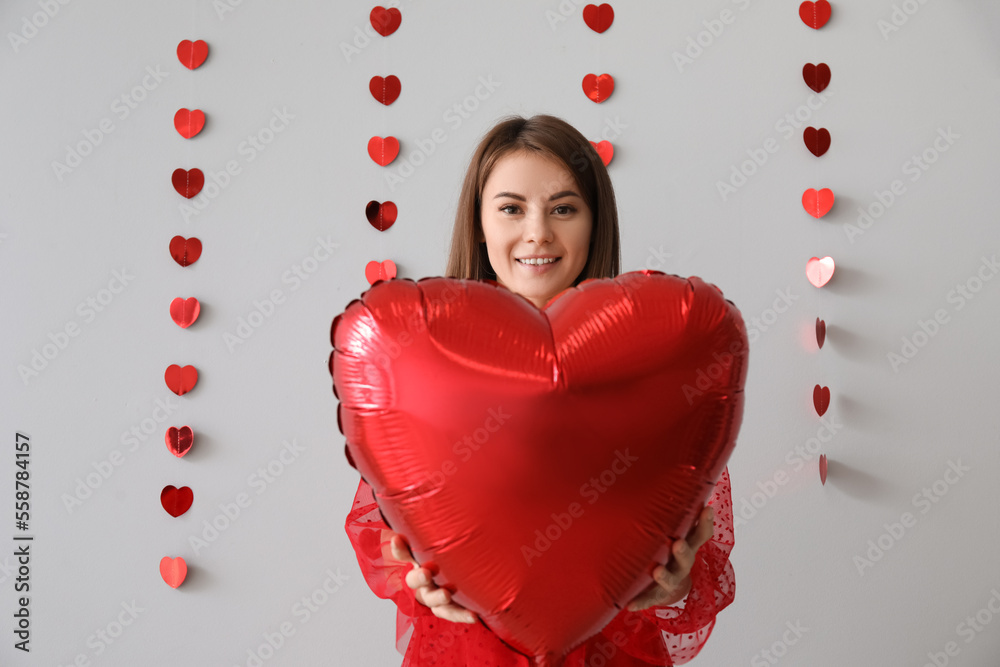 Young woman with balloon for Valentines Day on grey background