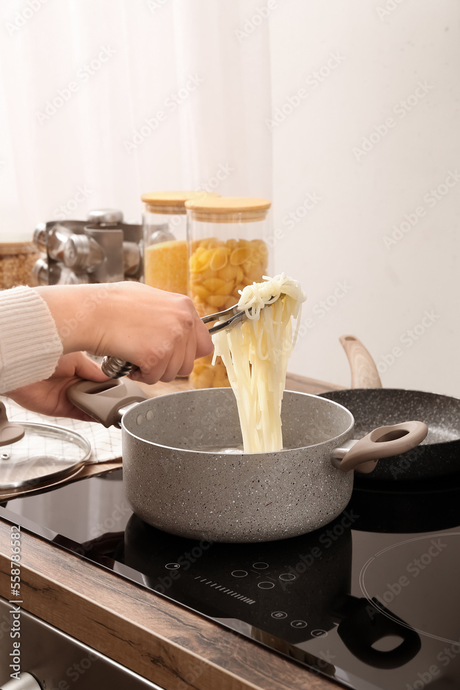 Woman preparing delicious pasta on electric stove in kitchen