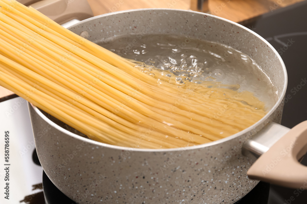 Cooking pot with raw pasta and boiling water on electric stove in kitchen