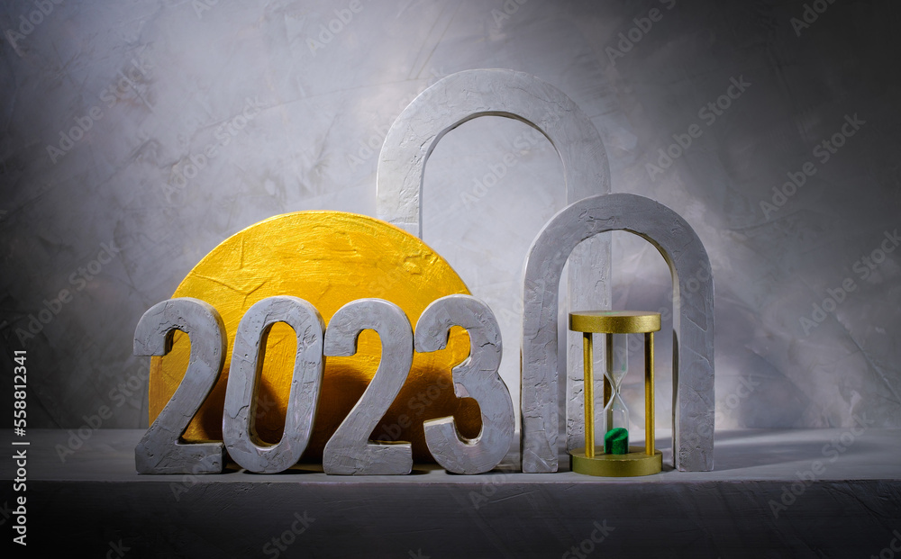 composition of numbers 2023 with gold geometric concrete and  hourglass on gray concrete wall backgr