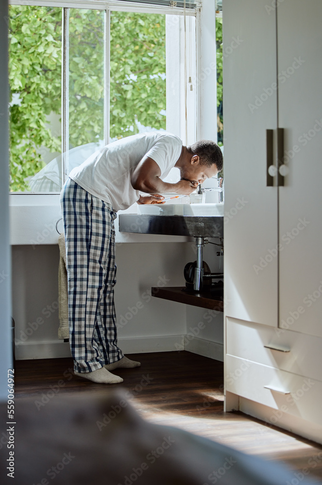 Black man brushing his teeth for dental health, hygiene or wellness in the bathroom of his home. Gro