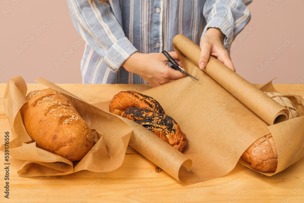 Woman cutting baking paper at table near pink wall