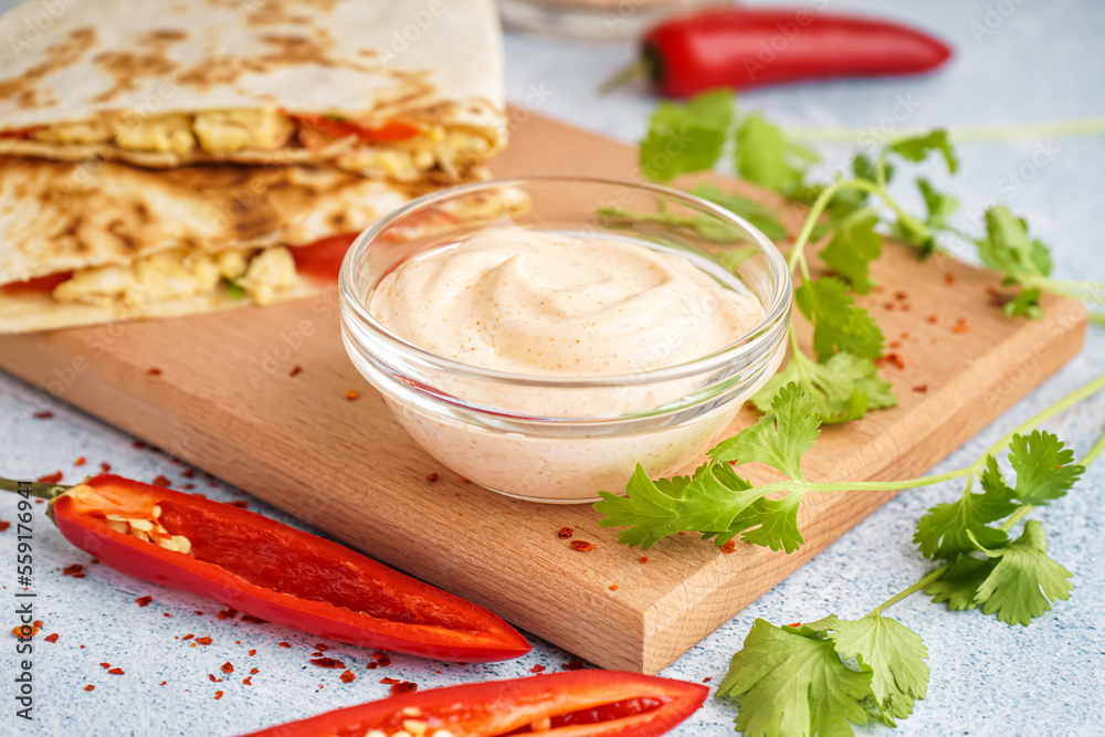 Wooden board with bowl of tasty chipotle sauce on table