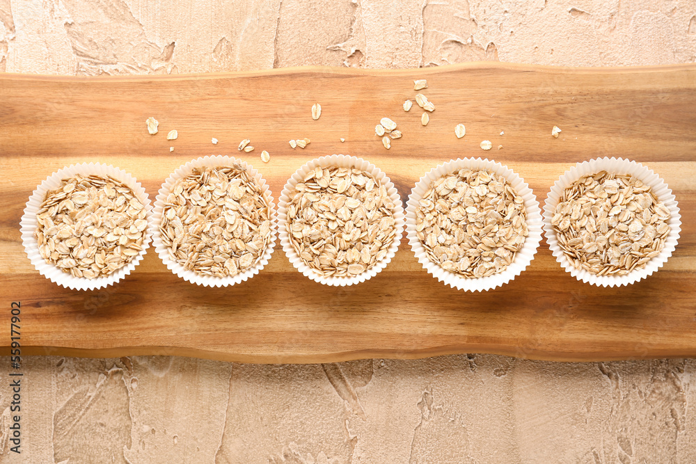 Wooden board with paper baking cups of raw oatmeal on color background