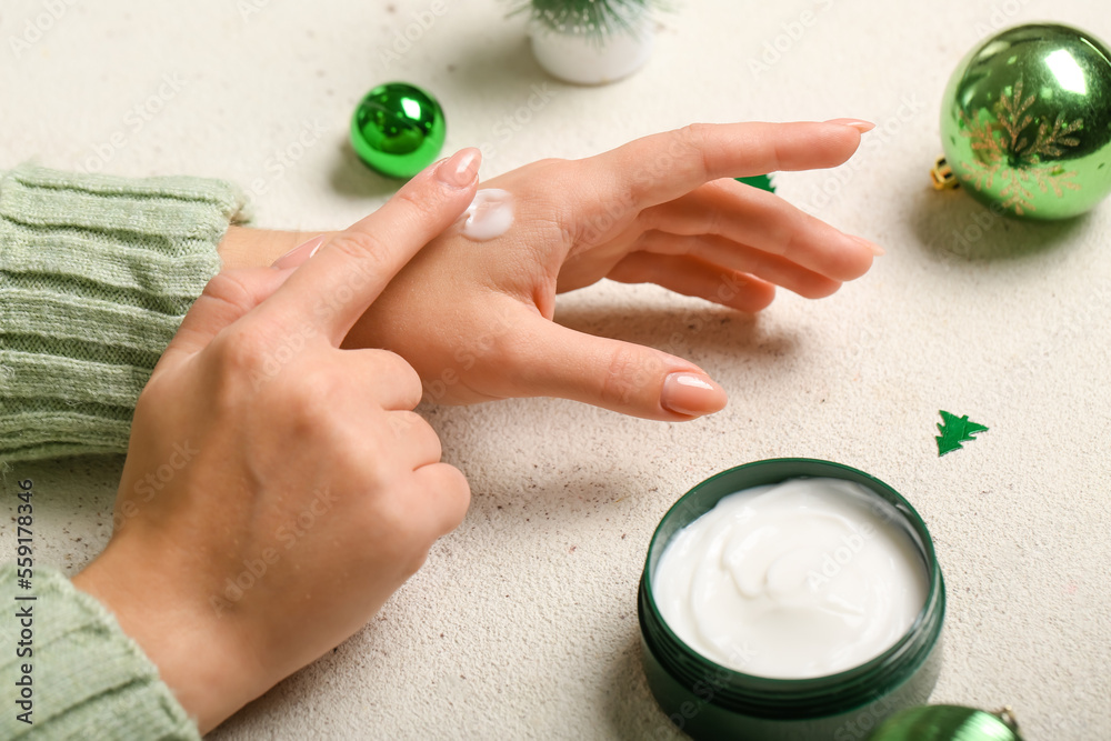 Woman applying cream onto hand on light background, closeup