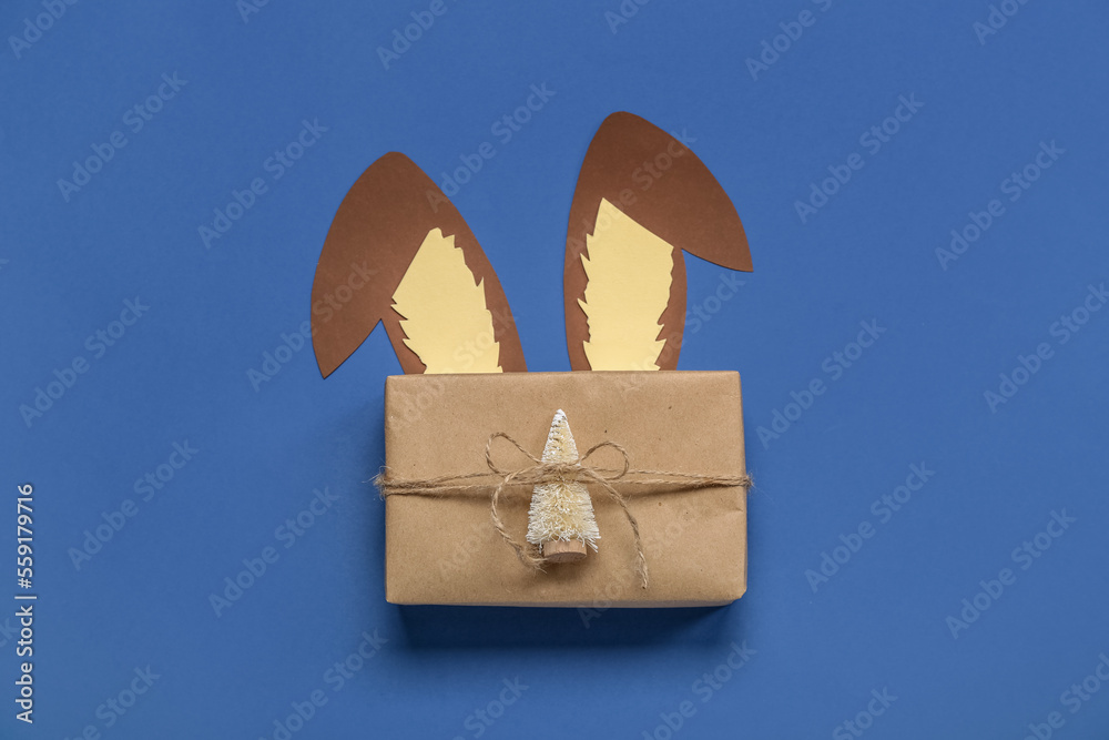 Paper bunny ears with Christmas gift on blue background