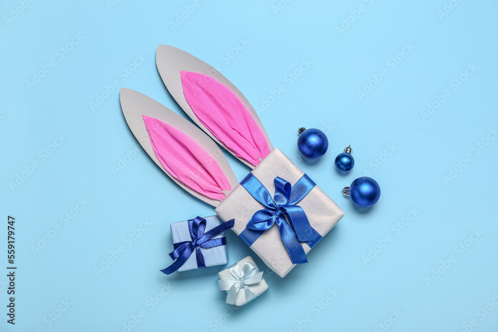 Paper bunny ears with Christmas balls and gifts on blue background