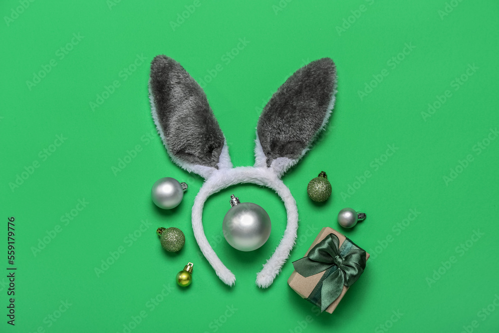 Bunny ears with Christmas balls and gift on green background