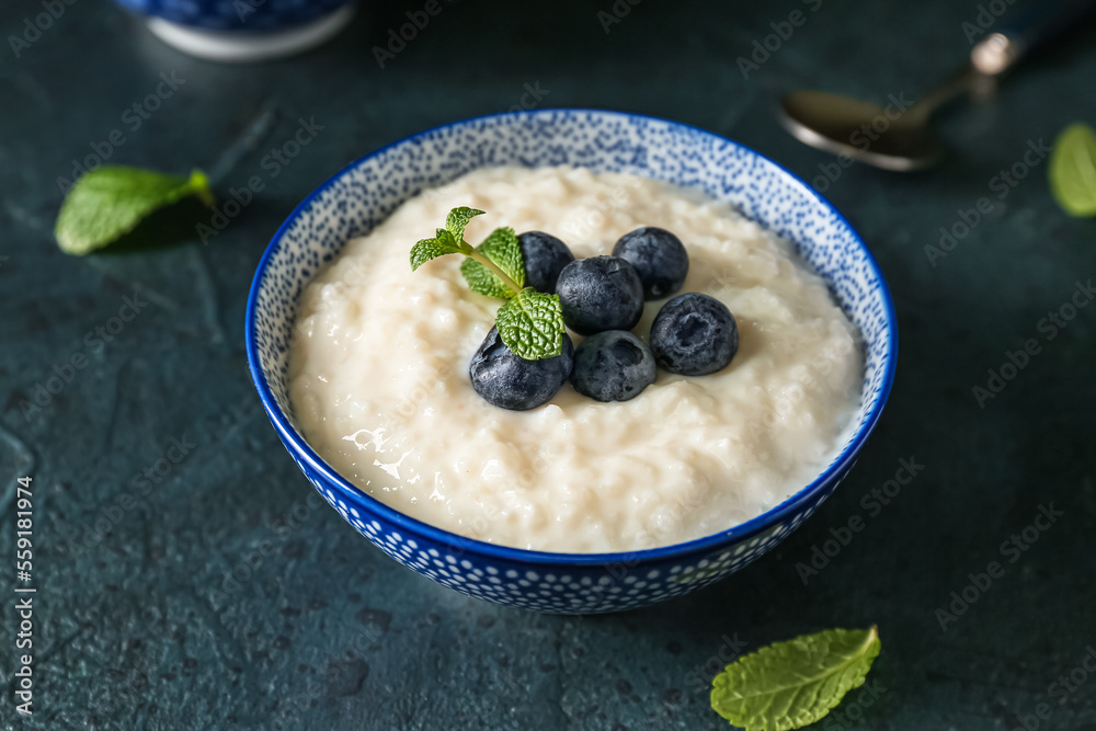 Bowl with delicious rice pudding and blueberries on black background