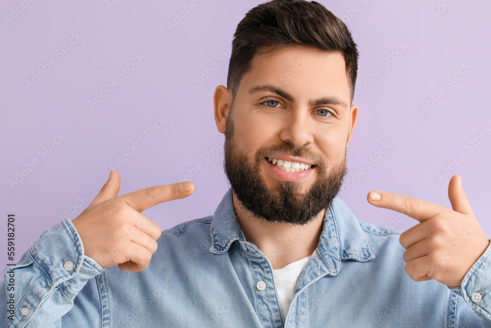 Young man pointing at his teeth on violet background, closeup