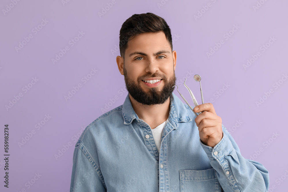 Young man with dental tools on violet background