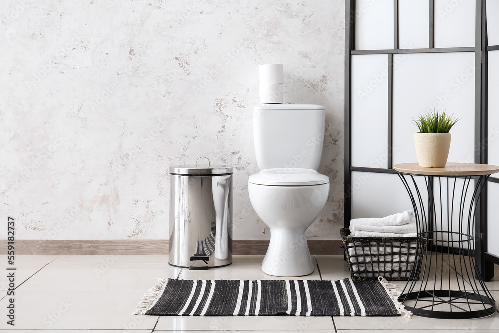 Interior of restroom with toilet bowl, table and folding screen