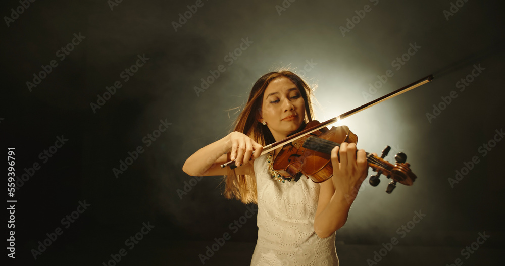 Female violin player performing sheet music on stage. Experienced asian violin player having solo co