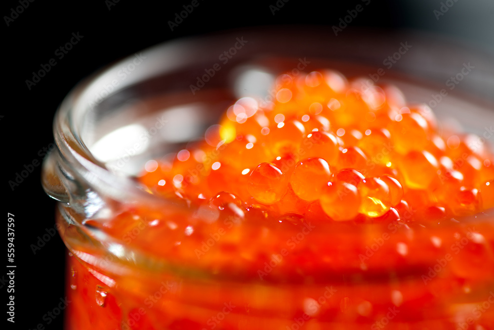 Red caviar in a glass jar, close up. Salmon caviar isolated on black background. Delicious gourmet f