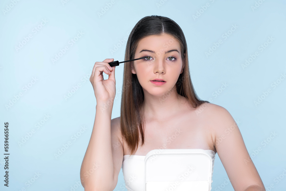 Closeup portrait of young charming applying makeup eyeshadow on her face with brush, mascara with fl