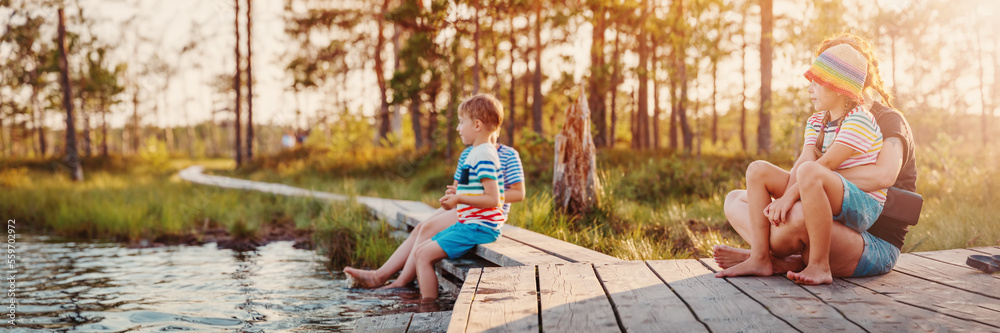 Mother with her children sitting on the pier of the swamp lake.