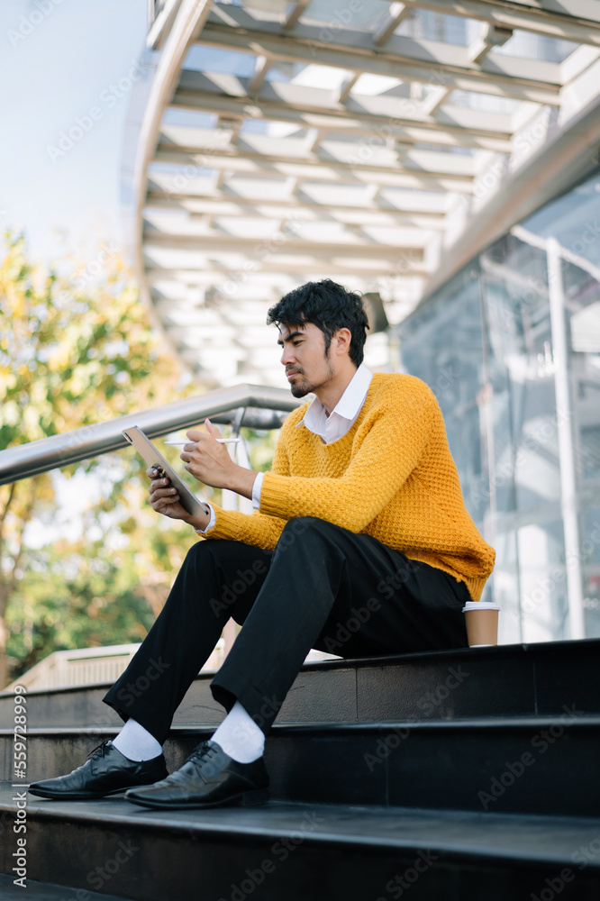 Entrepreneur holding and working on laptop, tablet while sitting at the urban street. Handsome busin