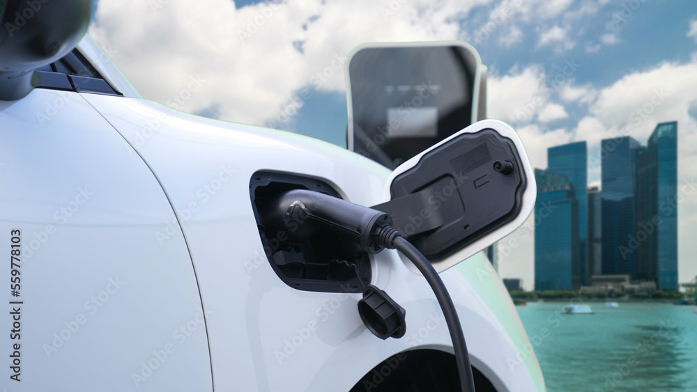 Electric vehicle, EV car recharges battery energy at charging station on the freeway in urban area s