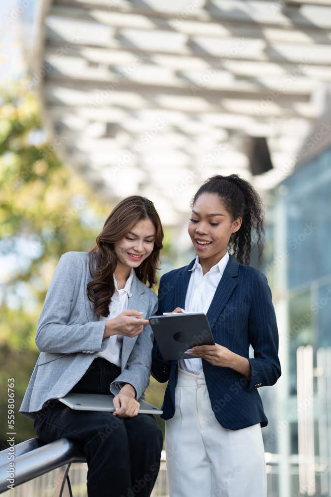 Two Asian businesswomen discussing business information while standing outside the office.