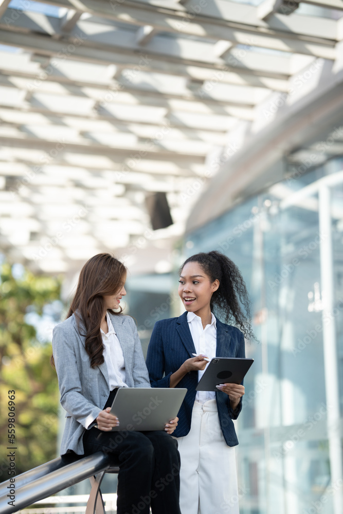 Two Asian businesswomen discussing business information while standing outside the office.