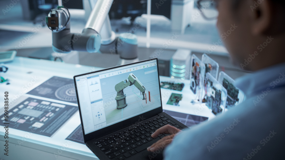 Over the Shoulder Shot of a Robotics Engineer Using a Laptop Computer with a Software Operating the 