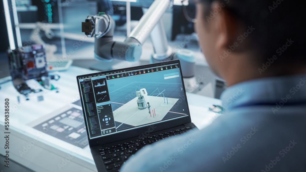 Over the Shoulder Shot of a Robotics Engineer Using a Laptop Computer with a Software Operating the 