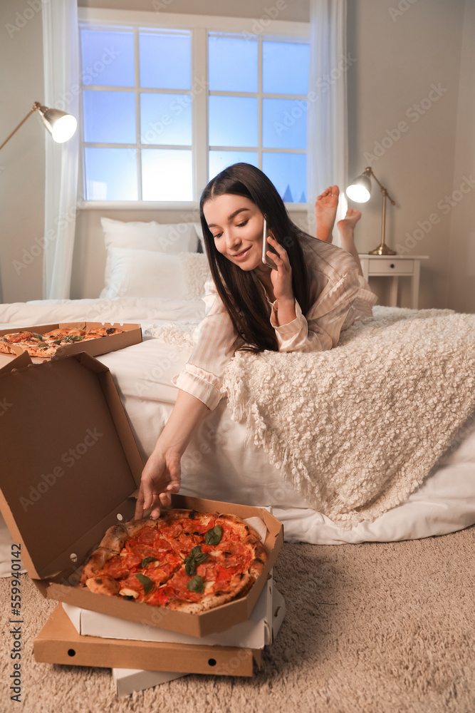 Young woman with tasty pizza in bedroom at night