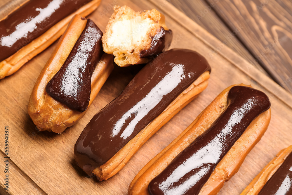 Wooden board with tasty chocolate eclairs, closeup