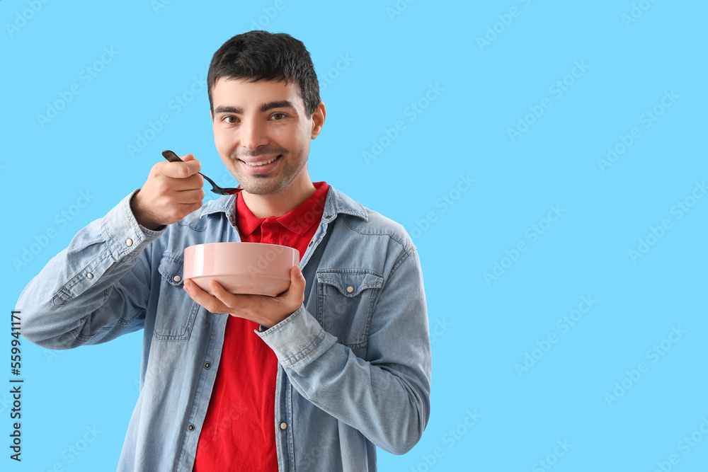 Young man with spoon and bowl on blue background