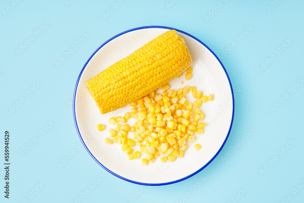 Plate with corn cob and kernels on blue background