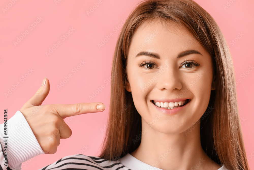 Young woman pointing at her teeth on pink background, closeup