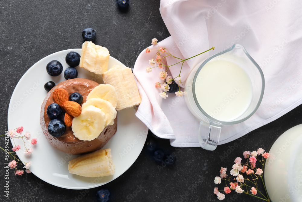 Plate with delicious chocolate pudding, almonds, blueberry, banana and glass of milk on black table