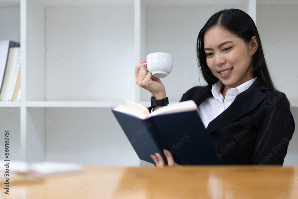 Portrait of an attractive and good-natured young Asian business woman drinking coffee while reading 