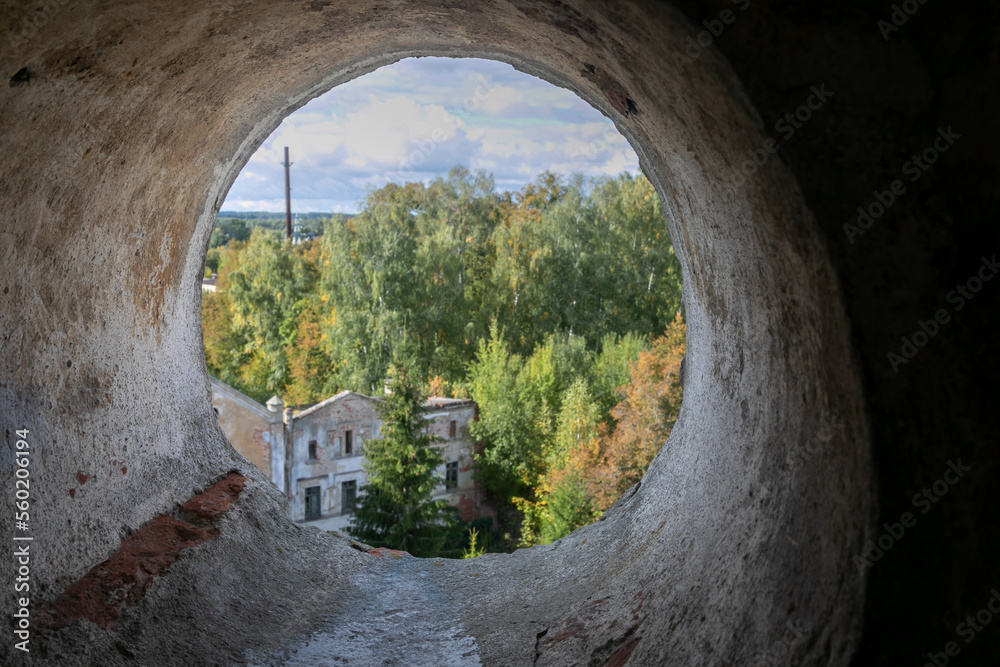 A large round hole in the shabby brick wall. View through a cement pipe to the countryside. In the d