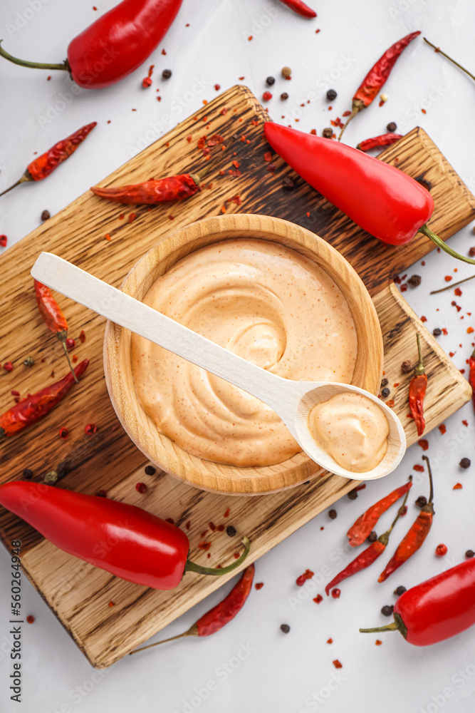 Wooden board with bowl of tasty chipotle sauce and spices on light background