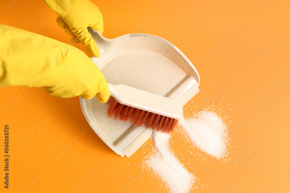 Woman in rubber gloves sweeping sugar with dustpan and brush on orange background