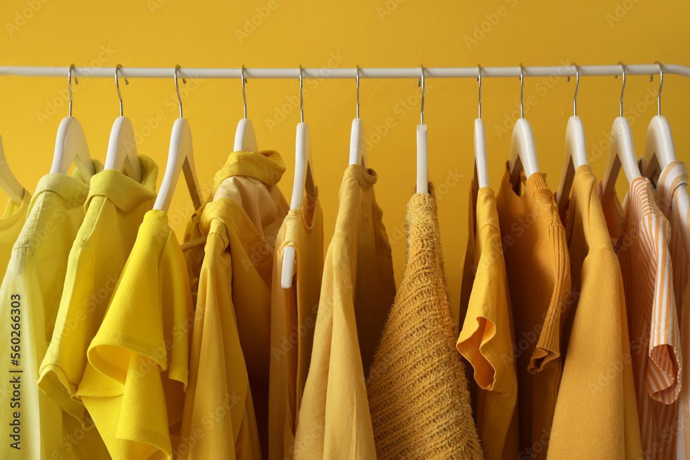 Rack with stylish female clothes near yellow wall, closeup