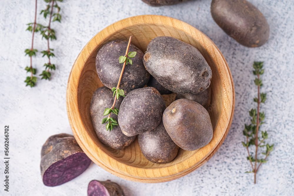 Wooden bowl of raw purple potatoes and thyme on light background