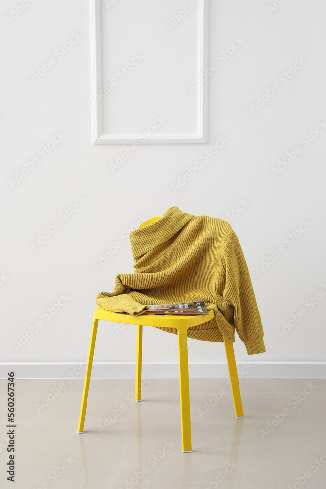 Chair with yellow sweater and magazine near light wall