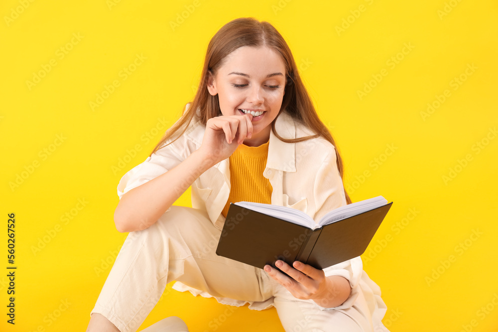 Young woman with book biting nails on yellow background