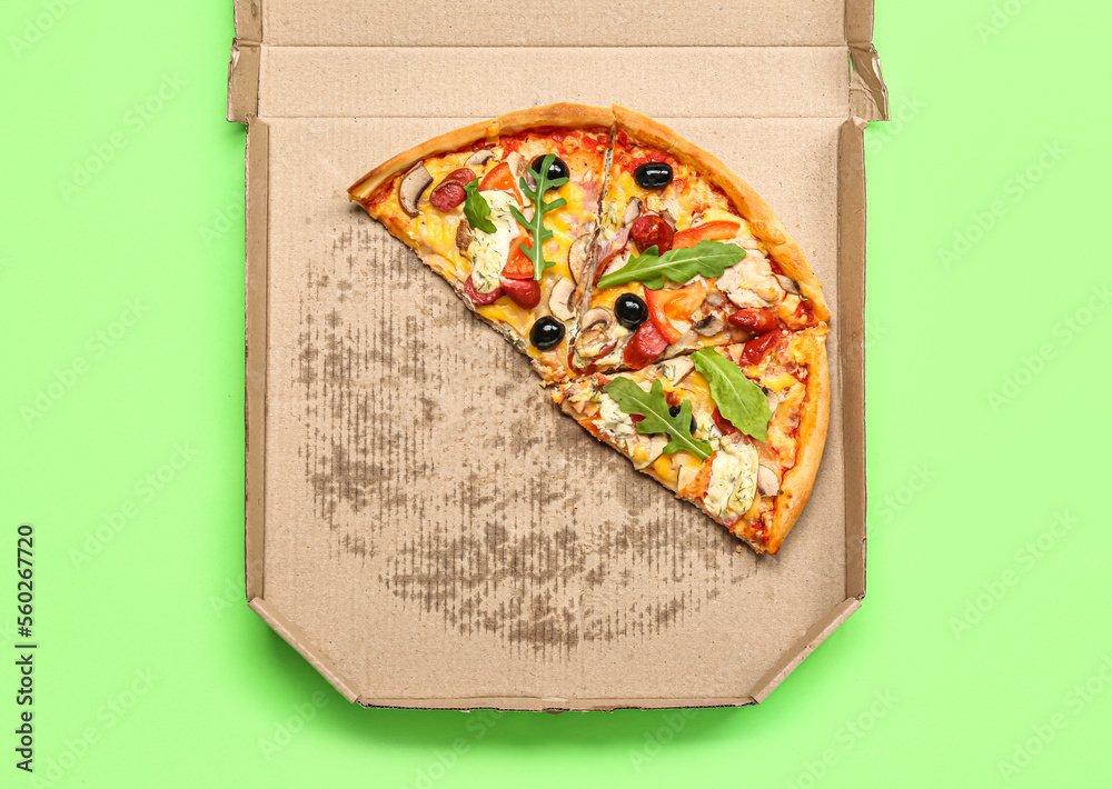 Cardboard box with delicious pizza on green background