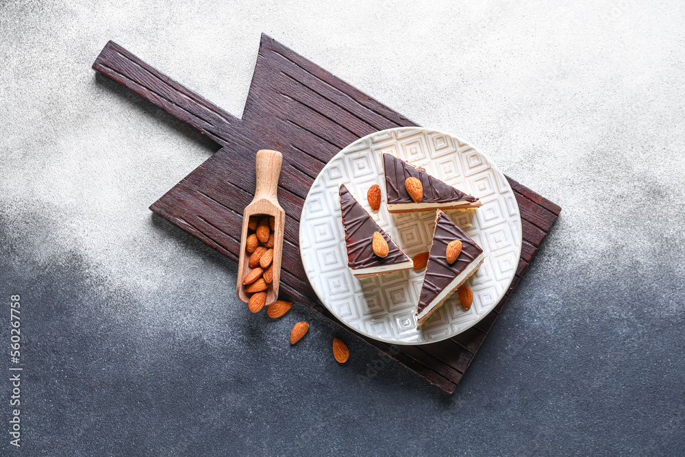 Board with plate of birds milk cake pieces, almond nuts and scoop on black and white background