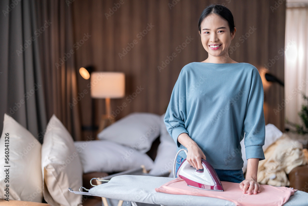 年轻的亚洲成年女性在家熨衣服，一个快乐女人熨衣服的肖像