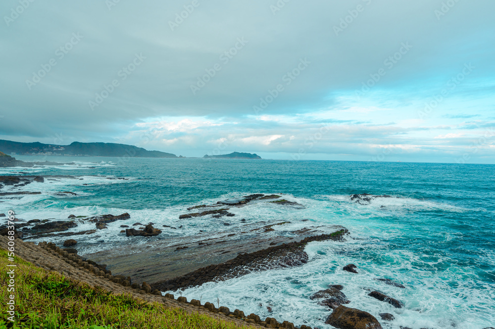 蓝天白云下的岩石海岸。白色的海浪和浅蓝色的大海。外木山海滨风景