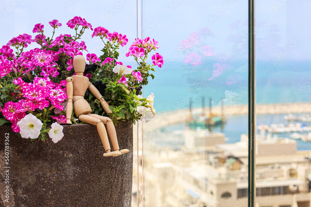 Wooden mannequin sitting in pot with flowers on balcony