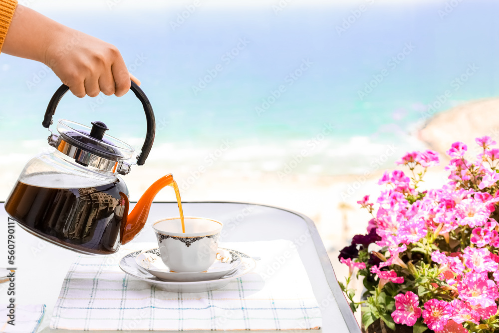 Woman pouring coffee into cup at table near window, closeup